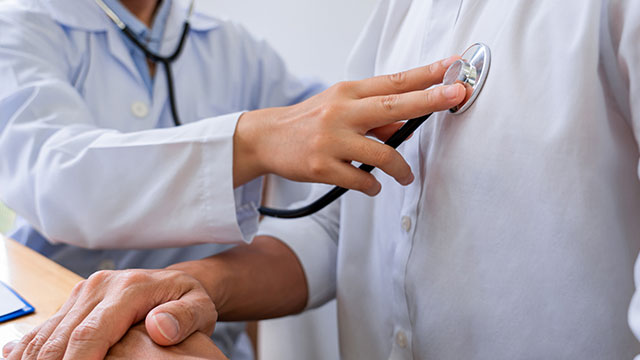 An elderly man receiving a medical check-up with a doctor using a stethoscope, set against a blurred background.